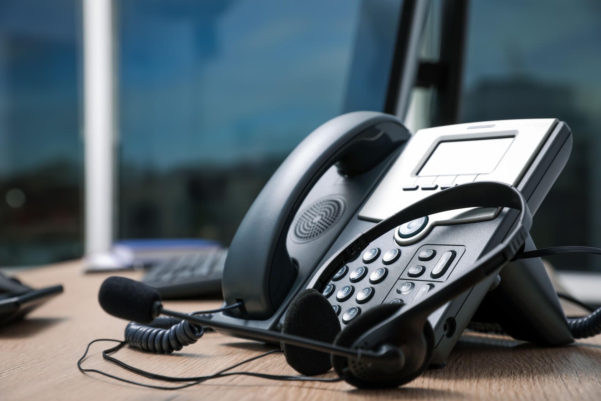 Stationary phone and headset on wooden desk indoors, closeup. Hotline service